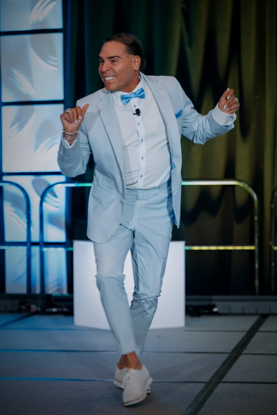 Dr. Rick Perea dancing on stage in a light-blue suit and bow tie