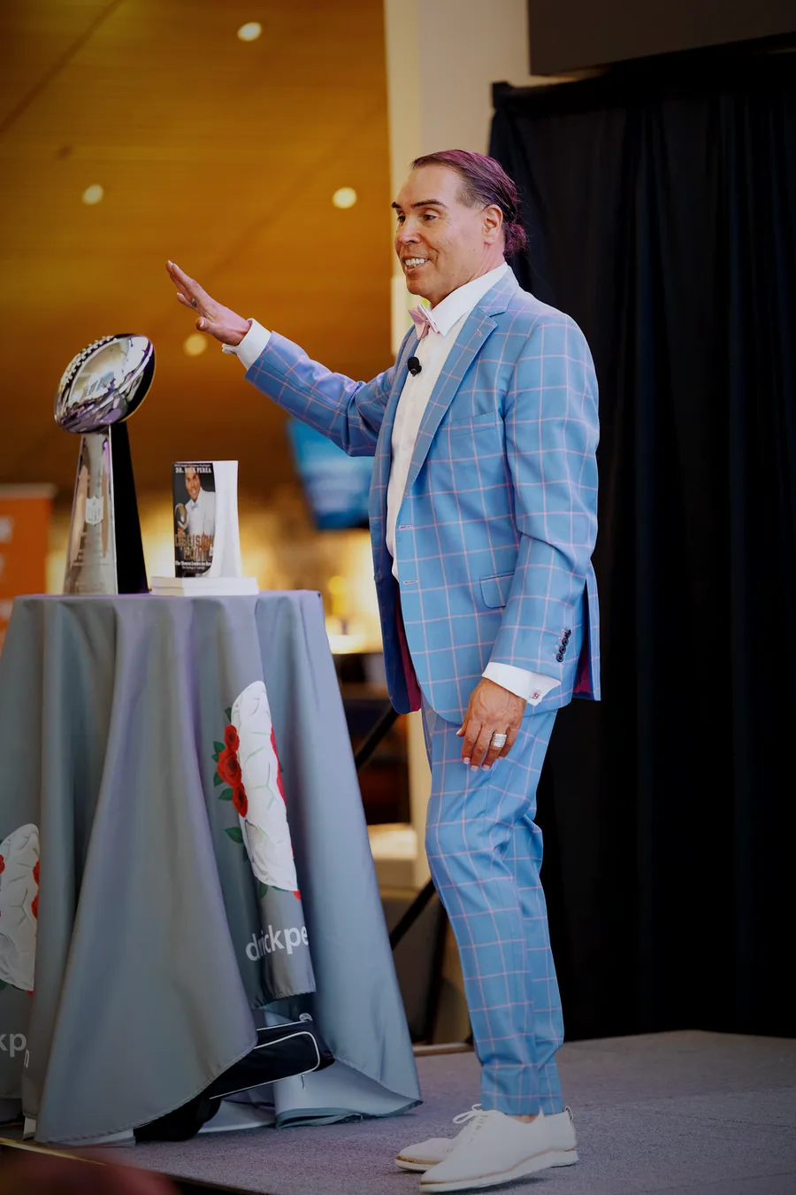 Dr. Rick Perea on stage beside the Super Bowl 50 Lombardi Trophy and his book