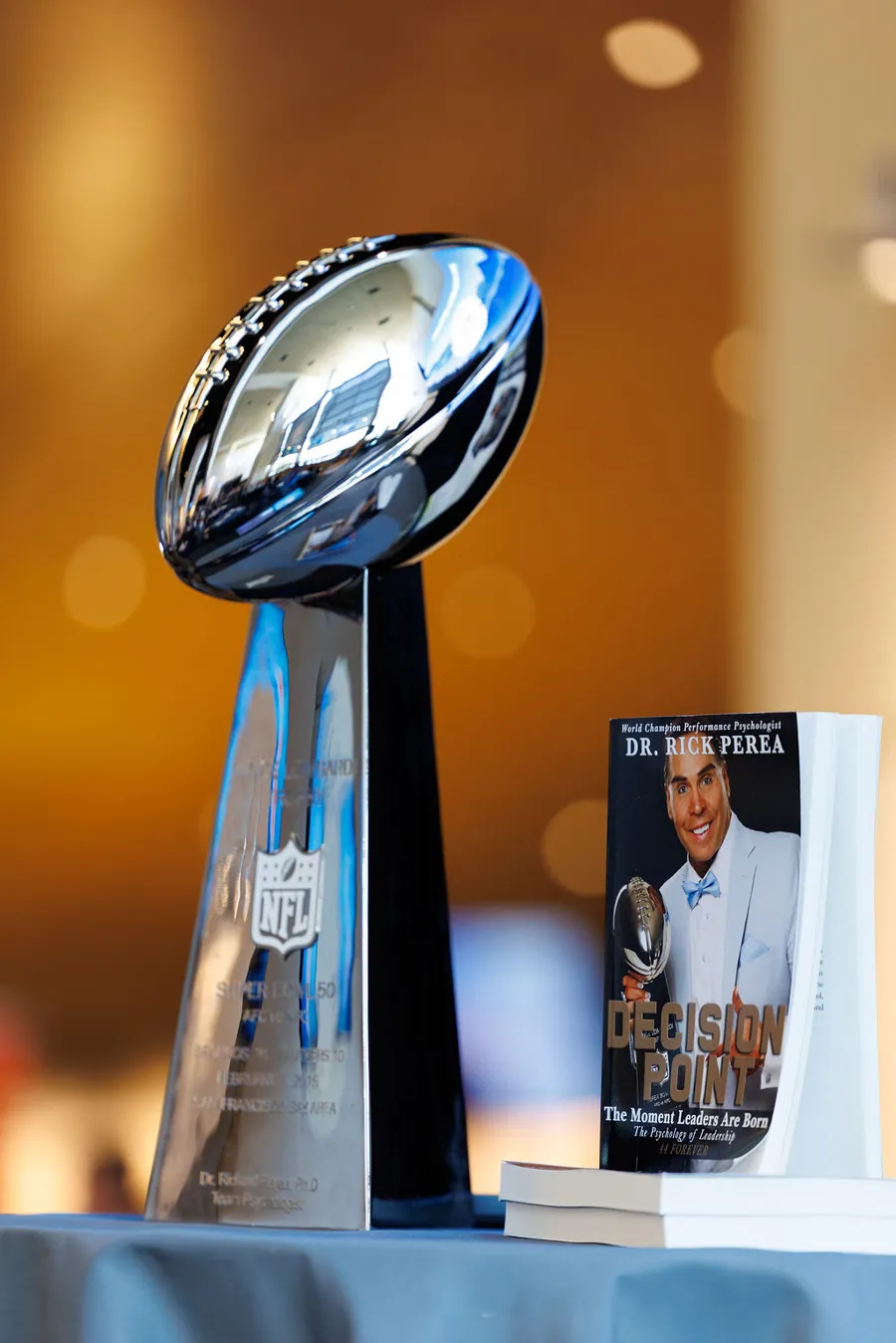 Super Bowl 50 Lombardi Trophy beside Dr. Rick Perea's book Decision Point